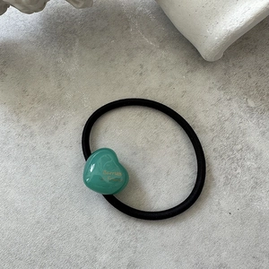 Close-up of a black elastic hair tie with a polished green resin heart-shaped accessory