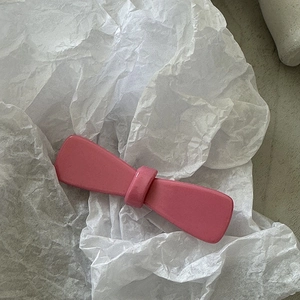 Détail d'une pince à cheveux rose mat en forme de nœud sur fond de papier blanc