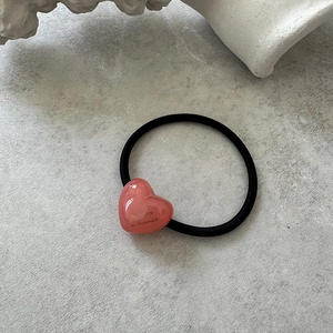 Detailed close-up of a pink heart hair tie with golden lettering on a stone background