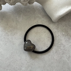 Detail of black elastic hair tie with grey resin heart charm and golden lettering