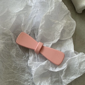 Gros plan de barrettes à nœuds rose mat sur papier blanc texturé avec détails fins