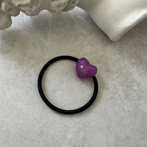 Detailed shot of purple heart-shaped hair tie on stone texture with golden Barrette text