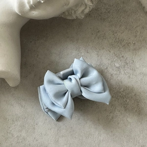 Détail d'une pince à cheveux avec nœud en satin bleu clair sur fond texturé
