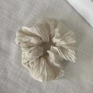 Détail de la texture plissée et de la forme ondulée du chouchou en tissu beige clair