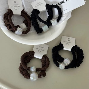 Detail view of coffee and black scrunchies with iridescent beads on a ceramic tray
