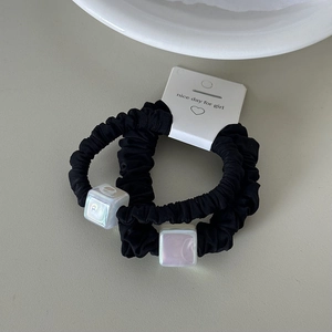 Detail of two black pleated hair ties with pearlescent square charms on white card
