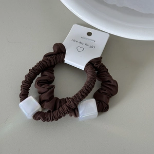 Detail view of two brown pleated scrunchies with white iridescent cube bead on card
