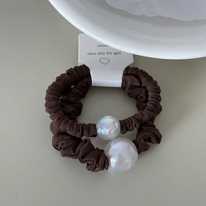 Detail of two coffee brown scrunchies with iridescent pearls on a white paper card