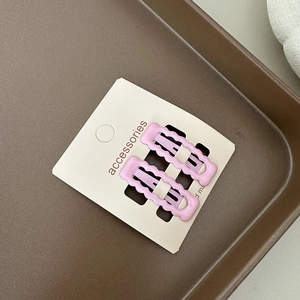 Gros plan de pinces à cheveux BB roses à bords ondulés sur une carte de présentation