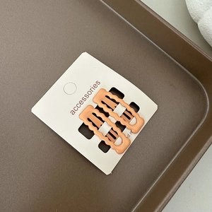 Détail de deux pinces à cheveux orange à bord ondulé sur une carte de présentation blanche