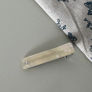 Close-up of cream rectangular hair clip with pearlescent finish and small rhinestone