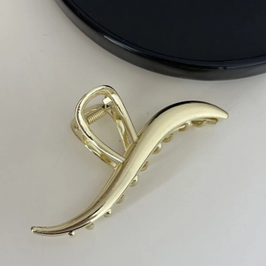 Macro detail of wave shaped gold metal hair claw clip with matte finish and spring mechanism