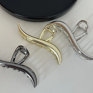 Detail of three large wave metal hair claws in gold, silver, and gunmetal finishes