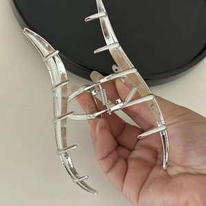 Close-up of a large silver wave metal hair claw clip being held to show its size and finish