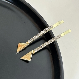 Detail of gold lucky triangle hair pins with rhinestones on a black plate surface