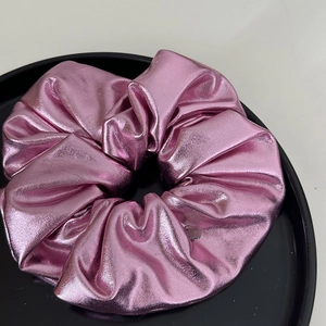 Détail d'un chouchou en cuir rose métallique sur plateau noir avec texture plissée