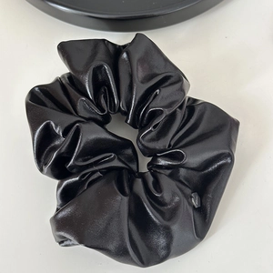 Détail du chouchou en cuir noir métallisé avec étiquette argentée et texture gaufrée