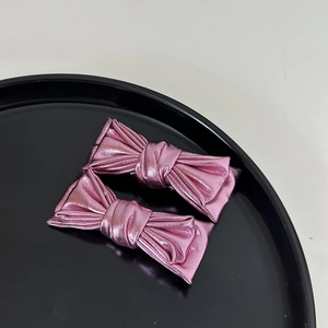 Vue macro détaillée de deux barrettes à nœuds en cuir rose métallisé sur plateau noir