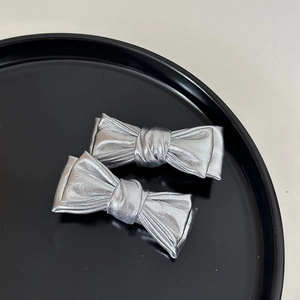 Détail de chouchous nœuds en tissu métallisé argenté avec texture plissée sur fond noir