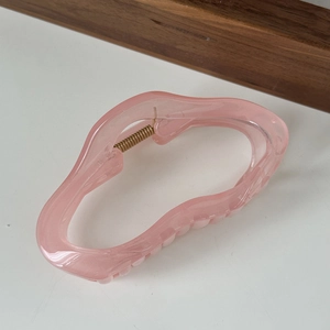 Detailed view of large translucent pink resin claw clip with wavy edge design and gold spring