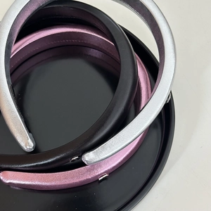 Trois serre-têtes épais en satin noir, argent et rose-violet posés sur un plateau