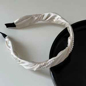 Détail du serre-tête ondulé en satin champagne orné de perles avec embouts de protection