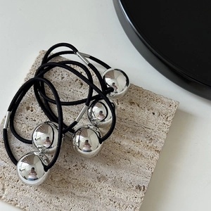 Close-up of four black elastic hair ties with polished silver mirror balls on stone plate