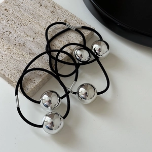 Close-up of three black elastic hair ties with polished silver metal spheres on stone