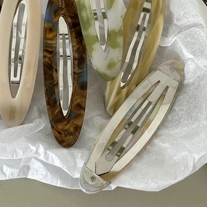 Detailed close-up of oval acetate hair clips in five colors on soft white crepe paper