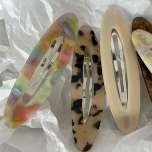 Close-up of four acetate oval hair clips with colorful marble patterns and handmade logo