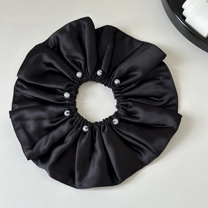Detail of a black satin scrunchie with eight white pearls on a minimalist white surface