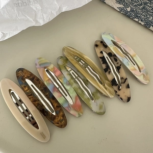 Elegant oval acetate hair clips in assorted tortoise and marble patterns on a beige setup