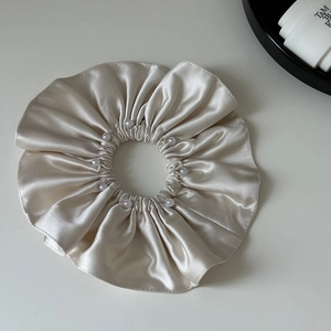 Detailed view of champagne satin scrunchie featuring elegant small white pearl accents