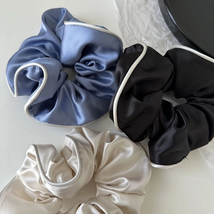 Three satin scrunchies in blue, beige, and black with delicate white piping edges