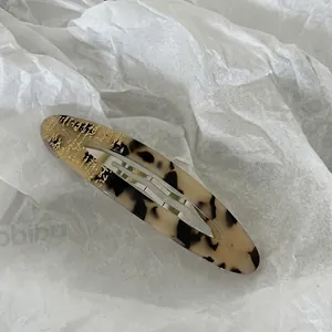 Detail view of oval tortoiseshell acetate hair clip with silver metal spring mechanism
