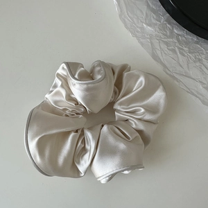 Detail view of the champagne satin fabric texture and pleated edge on the hair scrunchie