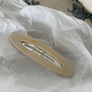 Detail view of oval beige acetate hair clip with metal BB snap on textured background