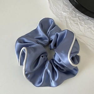 Detail of blue satin scrunchie featuring white contrast trim and smooth pleated texture