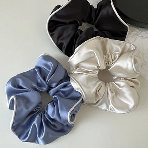 Detailed view of large satin scrunchies in black, cream, and blue with white piping edges