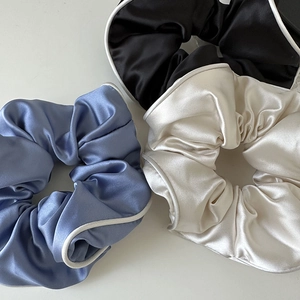 Detail view of large satin scrunchies in blue, white, and black with delicate stitching