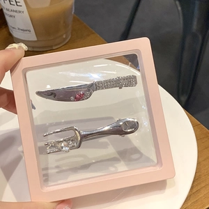 Detailed view of silver liquid metal knife and fork hair clips with crystals in a box