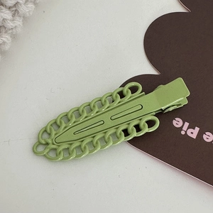 Détail de la pince à cheveux vert fruit en métal avec chaîne sur fond minimaliste