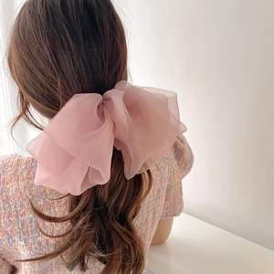 Detail view of tiered chiffon pink bow hair clip worn on long ponytail for elegant look
