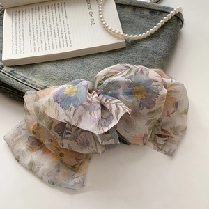 Detailed close-up of a large floral print chiffon bow hair clip on a stylized background
