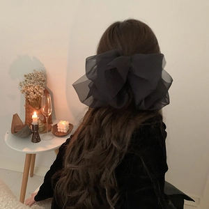 Detailed view of layered black organza bow hair clip on model's long wavy hair