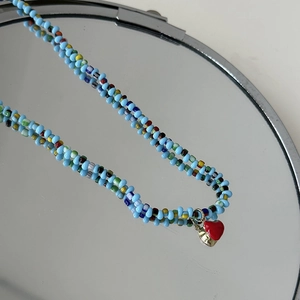 Détail d'un collier de perles colorées avec pendentif cœur rouge et bord doré