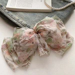 Detailed close-up of large floral chiffon bow hair clip on casual denim background