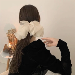 Close-up of a large cream ruffled chiffon scrunchie styled on long hair in a cozy setting
