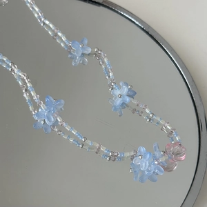 Gros plan du collier de perles pastel avec fleurs bleu clair sur fond de miroir