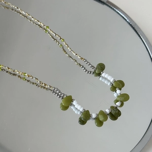 Gros plan d'un collier de perles avec pendentif vert et détails argentés sur miroir poli